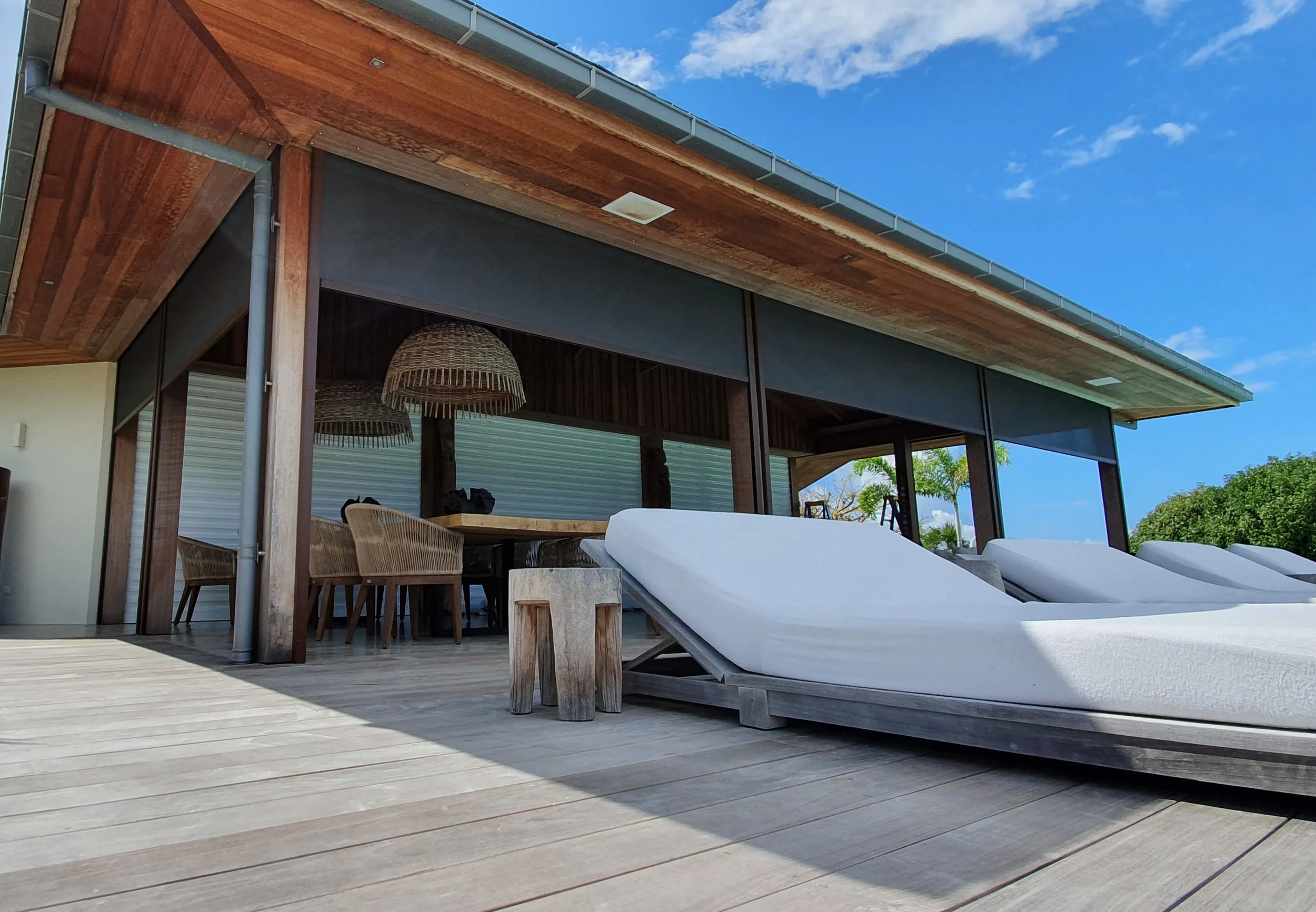 Outdoor patio area with lounge chairs, a wooden table, and custom electric vertical stores.