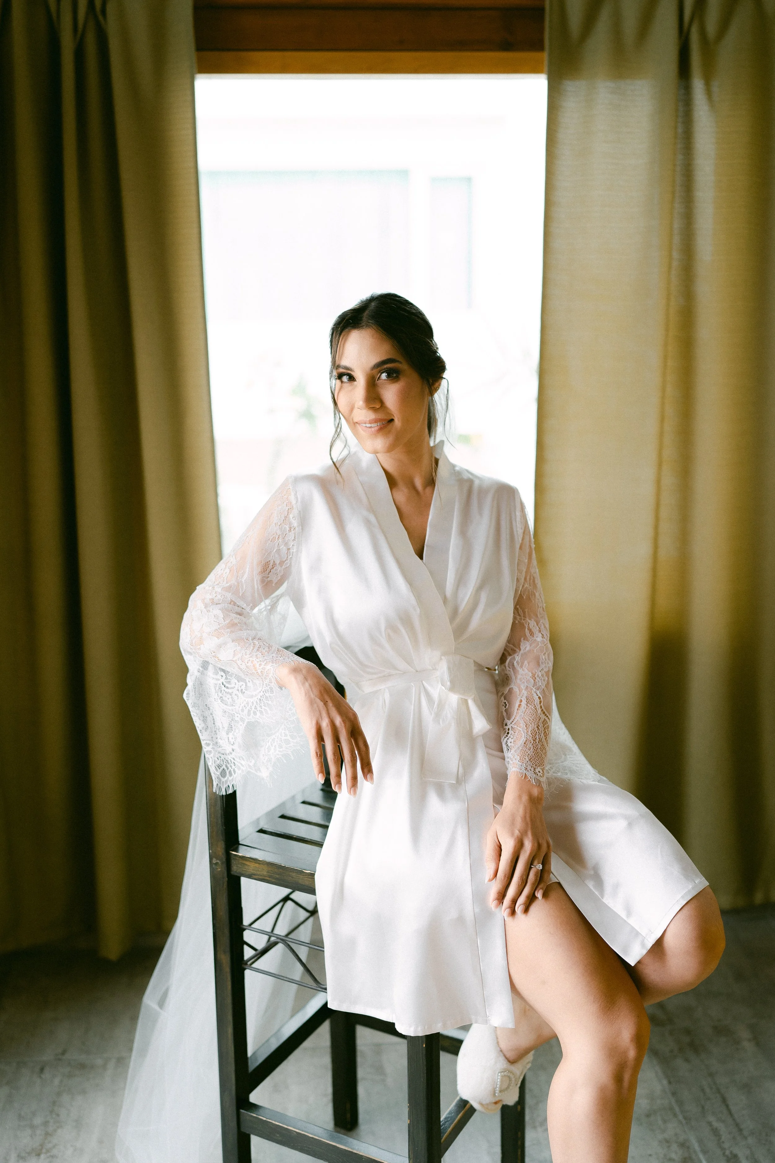 Mujer con vestido de novia sentado en una silla junto a una ventana.