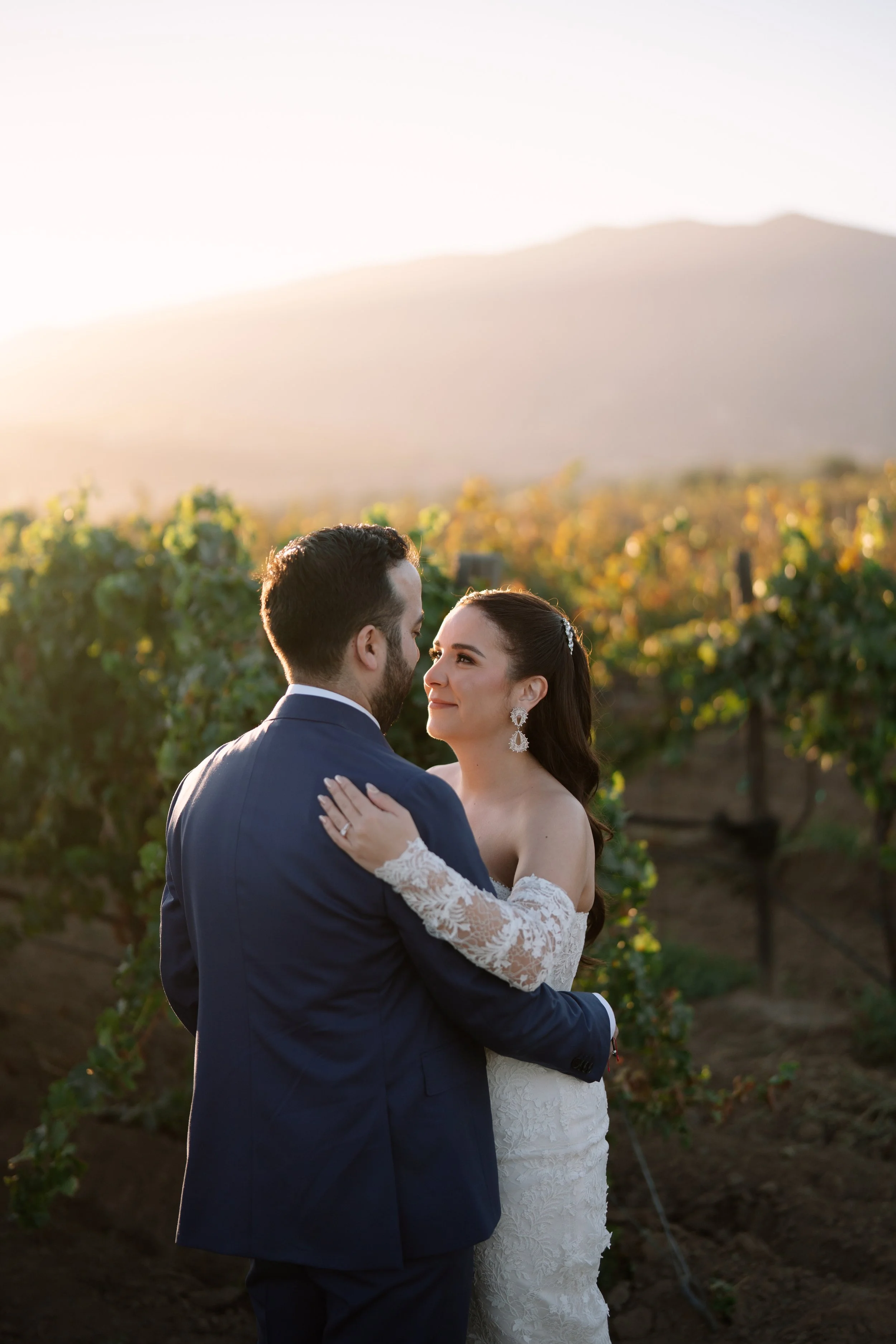 Una pareja de novios en un campo de viñedos durante el atardecer, en un momento romántico y feliz.