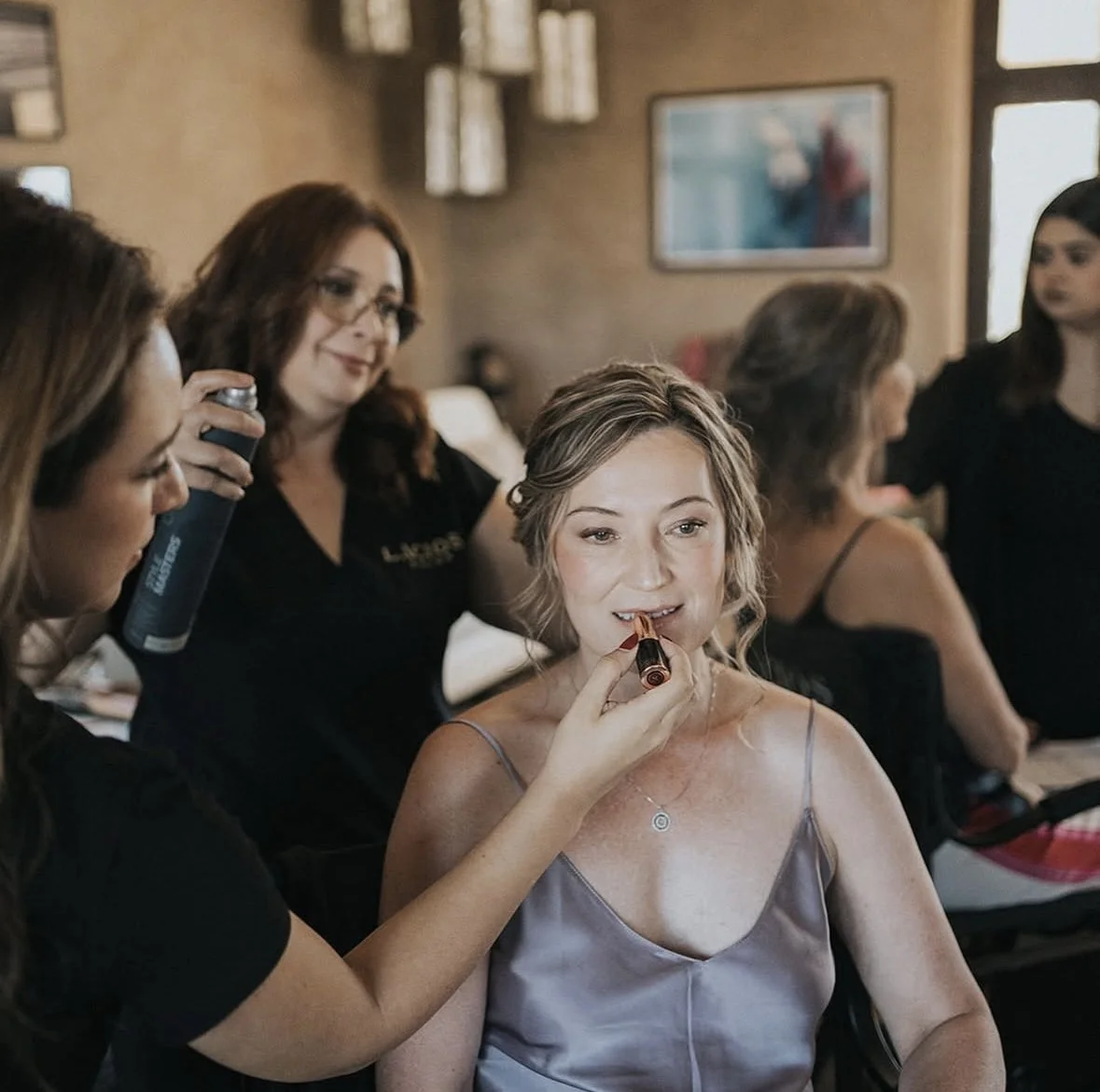 Mujer con vestido lila y maquillaje en proceso en una reunión de estilistas en un salón de belleza.