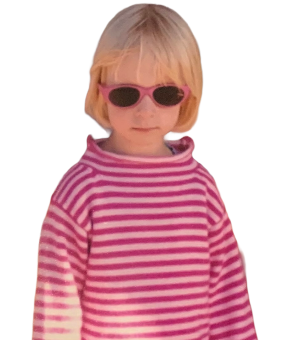 A young girl with blond hair wearing pink sunglasses and a pink and white striped turtleneck sweater.