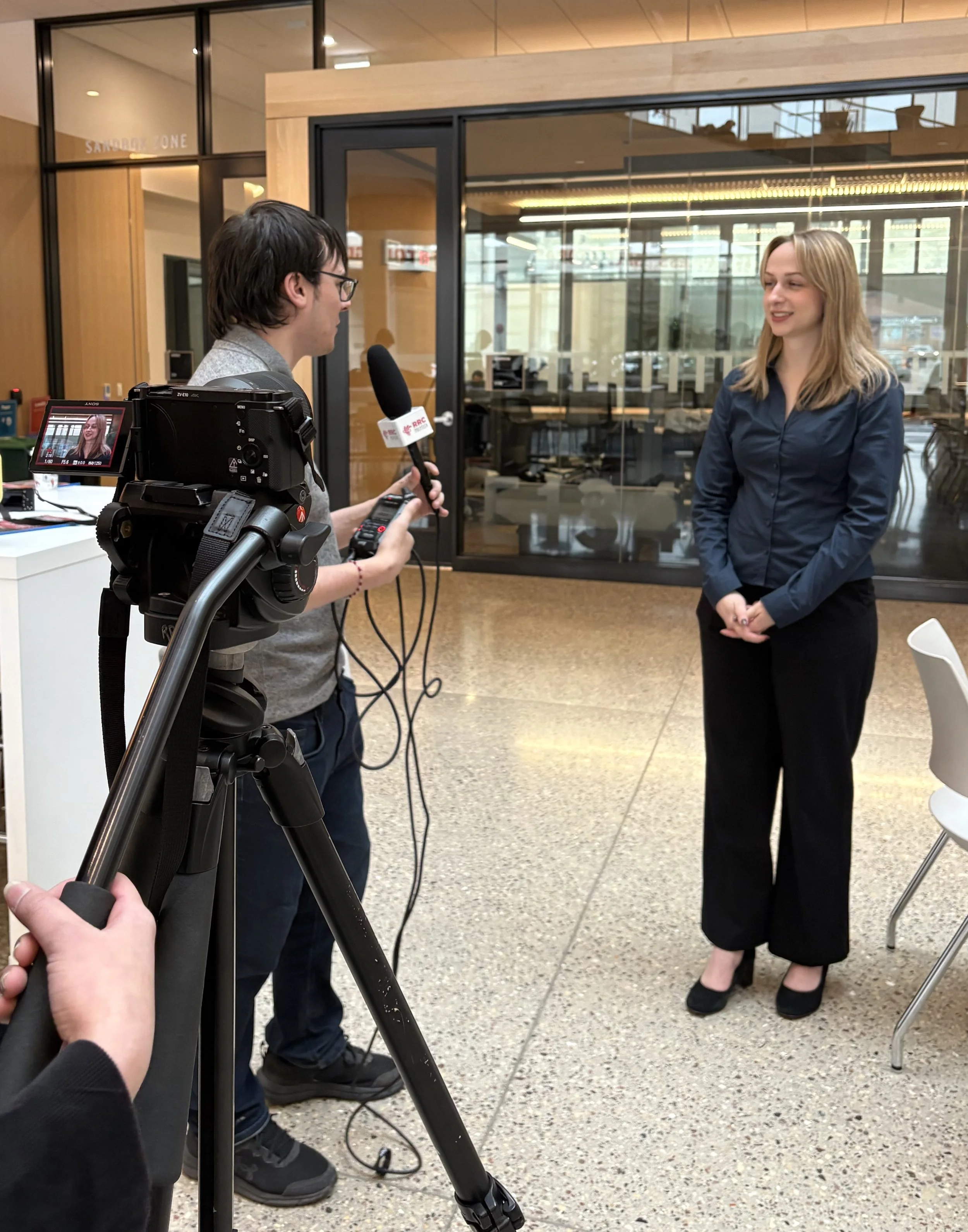 A woman being interviewed by a man with a video camera in an indoor setting.