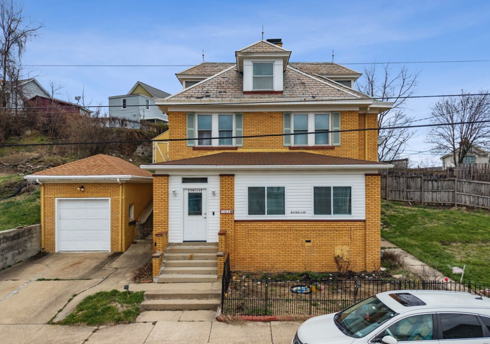Multi-story house with brick and white siding exterior, front steps, a garage, and a parked car in the driveway.