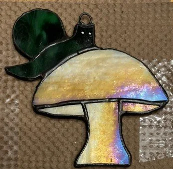 A stained glass sun catcher of a mushroom with a green hat, set against a textured background.