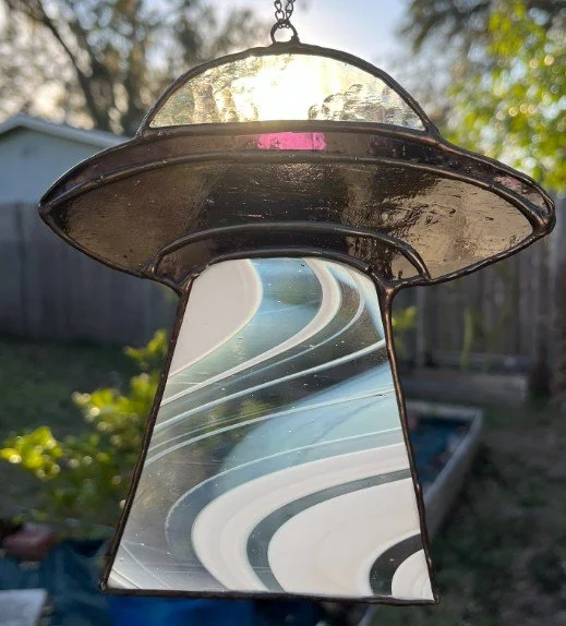 Stained glass spaceship in purple with abstract swirl patterns, hanging outdoors in sunlight.
