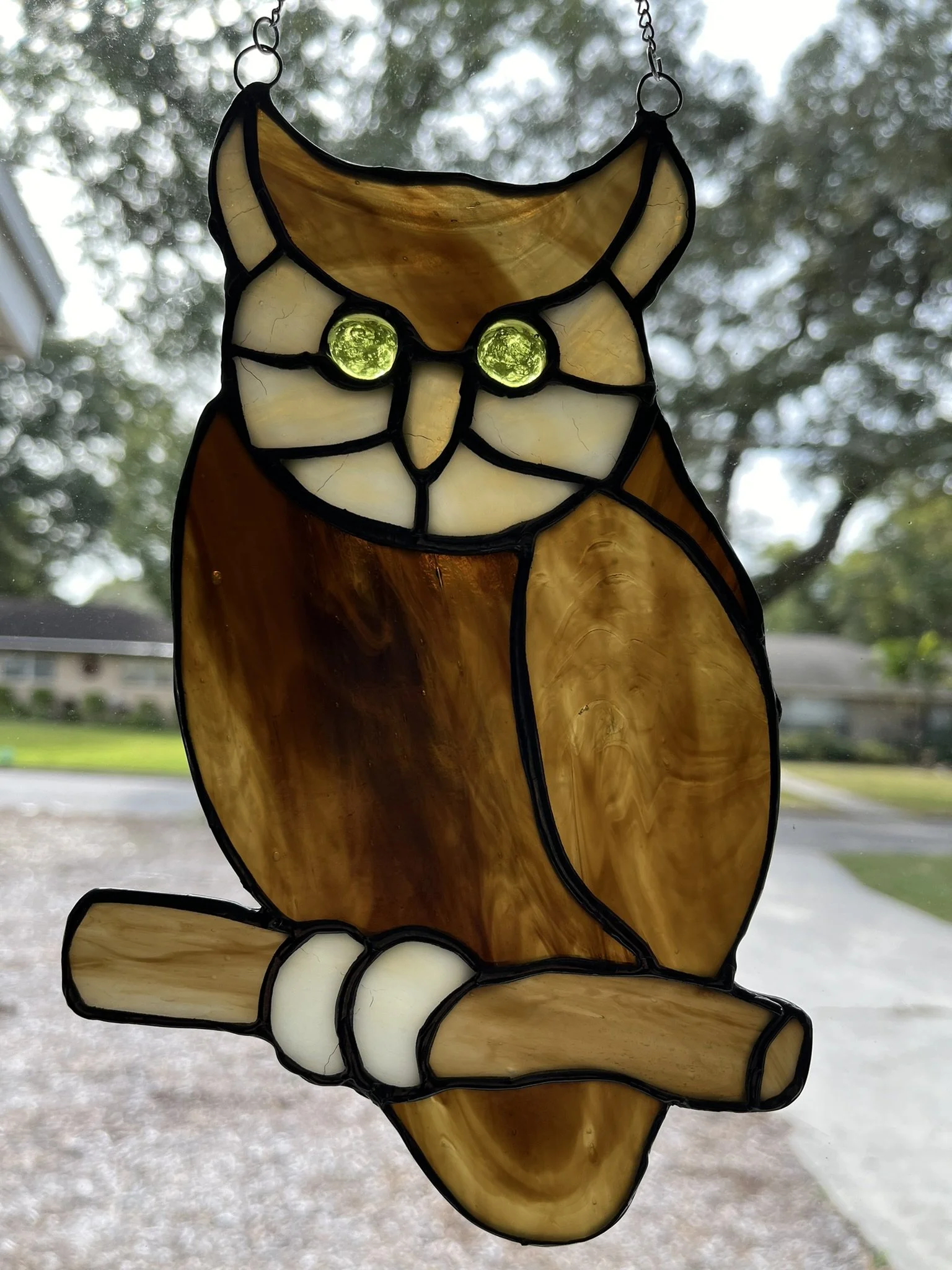 Stained glass sun catcher of an owl sitting on a branch with green eyes.