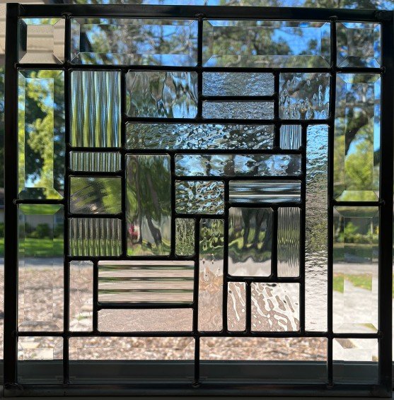 Decorative window with stained glass and black frame, reflecting trees and sky outside.