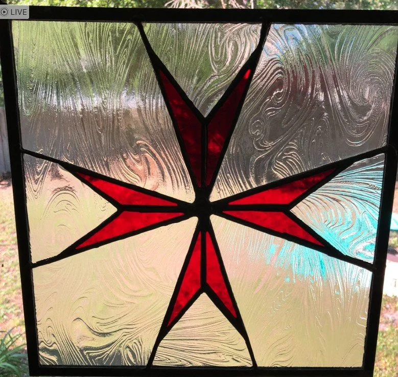 Stained glass window featuring a red and black Maltese Cross with textured glass background.