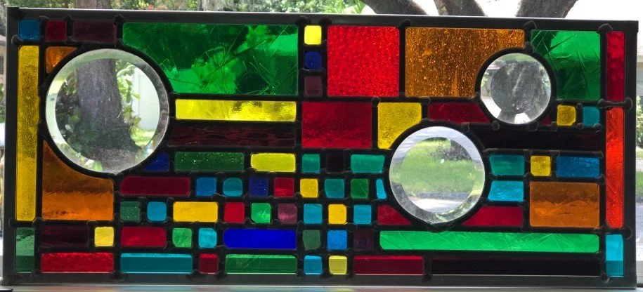 Colorful stained glass panel with circles and rectangular shapes in green, red, yellow, blue, and orange.