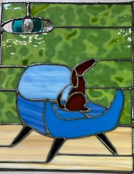 Colorful stained glass window depicting a dog sleeping in a blue armchair with a green background and a hanging lamp in the top left corner.