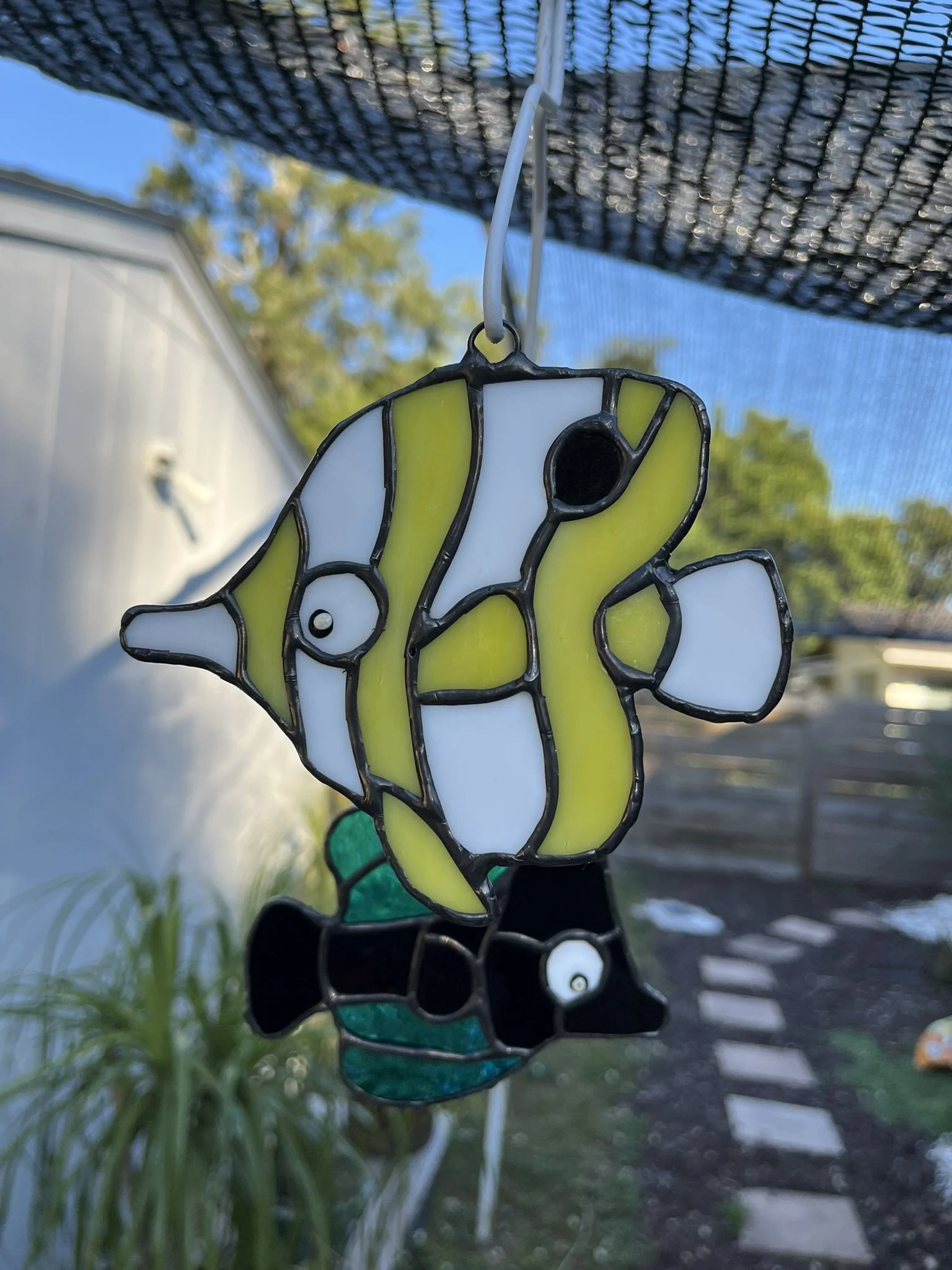 A stained glass decoration of a yellow and white clownfish with black accents hanging outdoors.