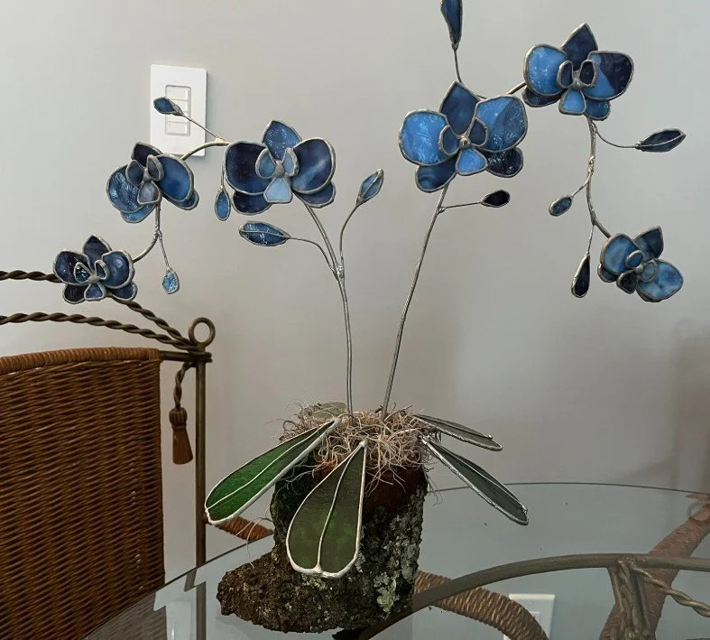 Decorative blue double stem orchid flower sculpture with green leaves in a wooden stump.
