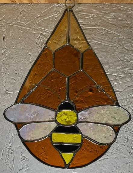 Stained glass art piece in the shape of a honeybee with amber and yellow colors.