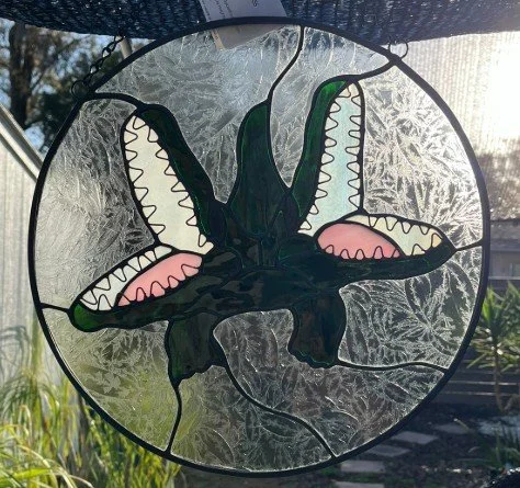 Seminole Heights Two Headed Gator stained glass window with green and pink accents, hanging outdoors with sunlight shining through.