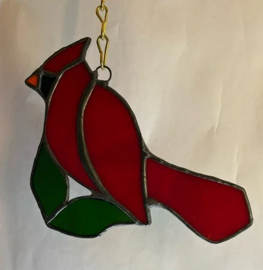 Stained glass decoration of a cardinal bird with red, black, orange, and green glass pieces, hanging from a chain.