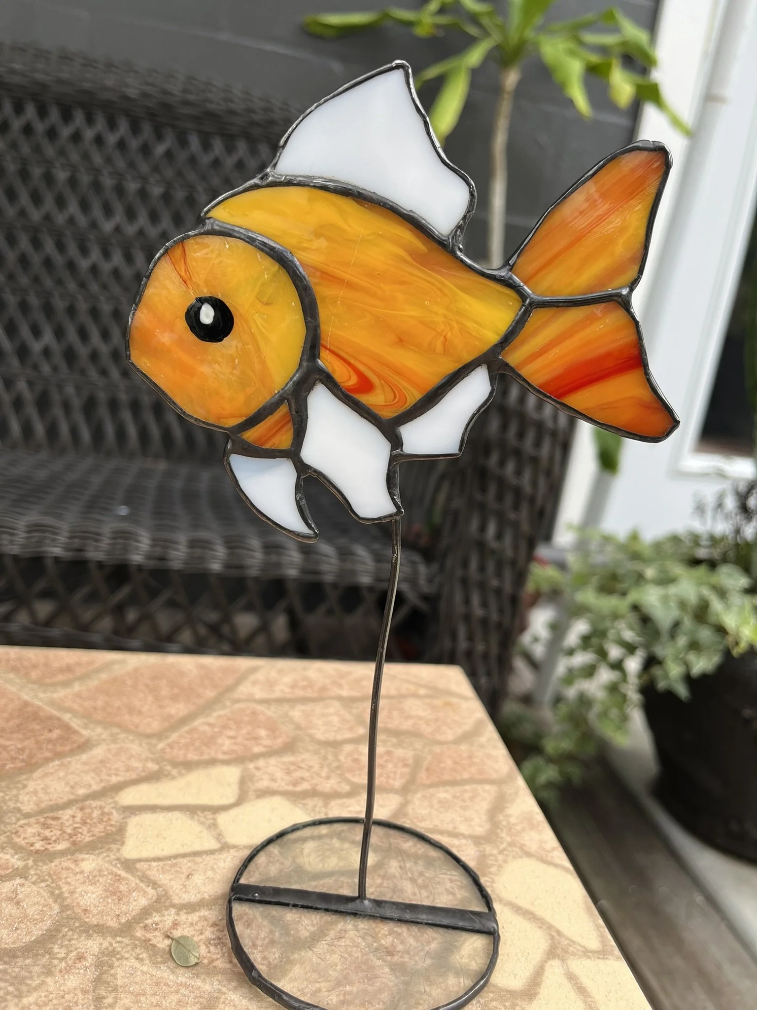 Colorful stained glass goldfish sculpture with orange, yellow, and white glass, on a metal stand.
