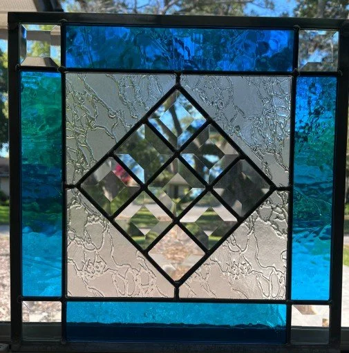 Decorative stained glass window with a diamond-shaped central design, featuring textured clear and blue glass panels.