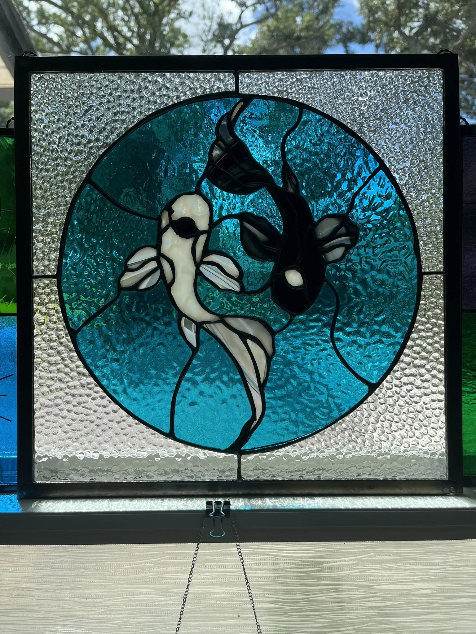 Stained glass art depicting a koi fish yin yang with a black and white fish, surrounded by textured blue and clear glass.
