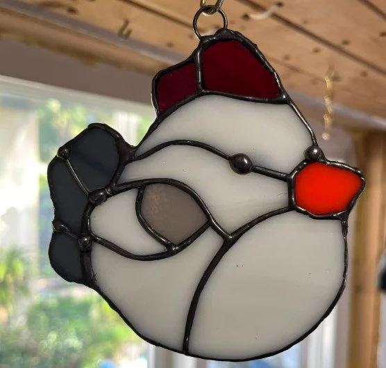 A stained glass sun catcher art piece of a Chickadee, with various colored glass pieces including red, black, white, gray, and orange.