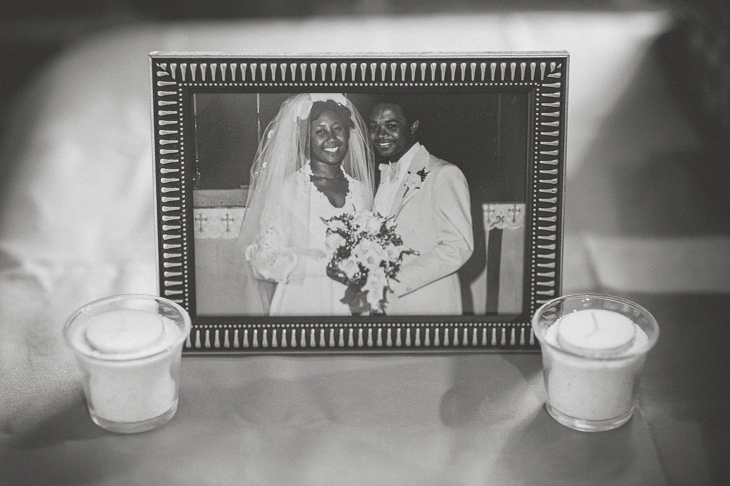 A framed black and white photo of a bride and groom on their wedding day, with two lit candles on either side, placed on a table.