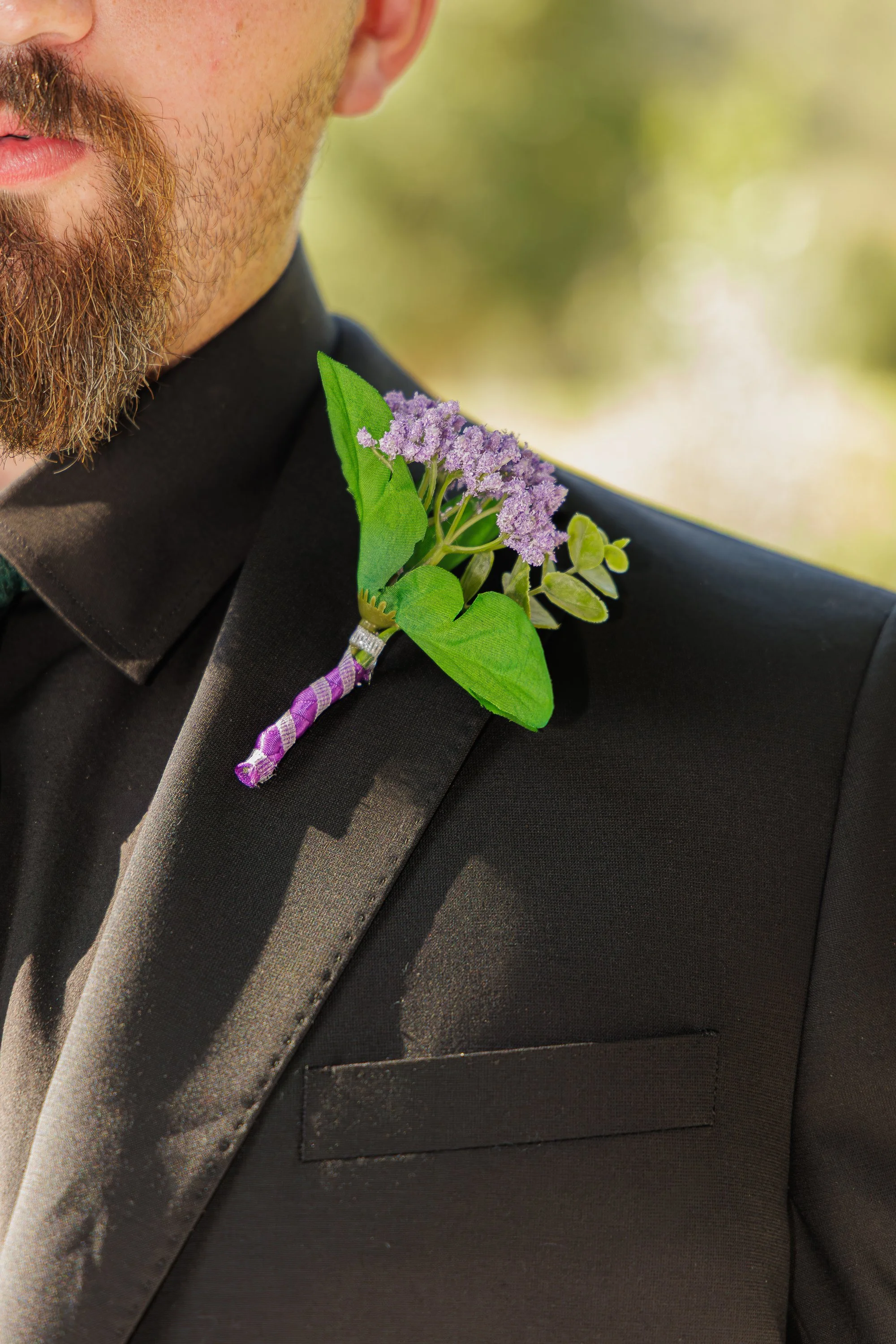 Close-up of a man wearing a black tuxedo with a purple and white boutonniere on the lapel.