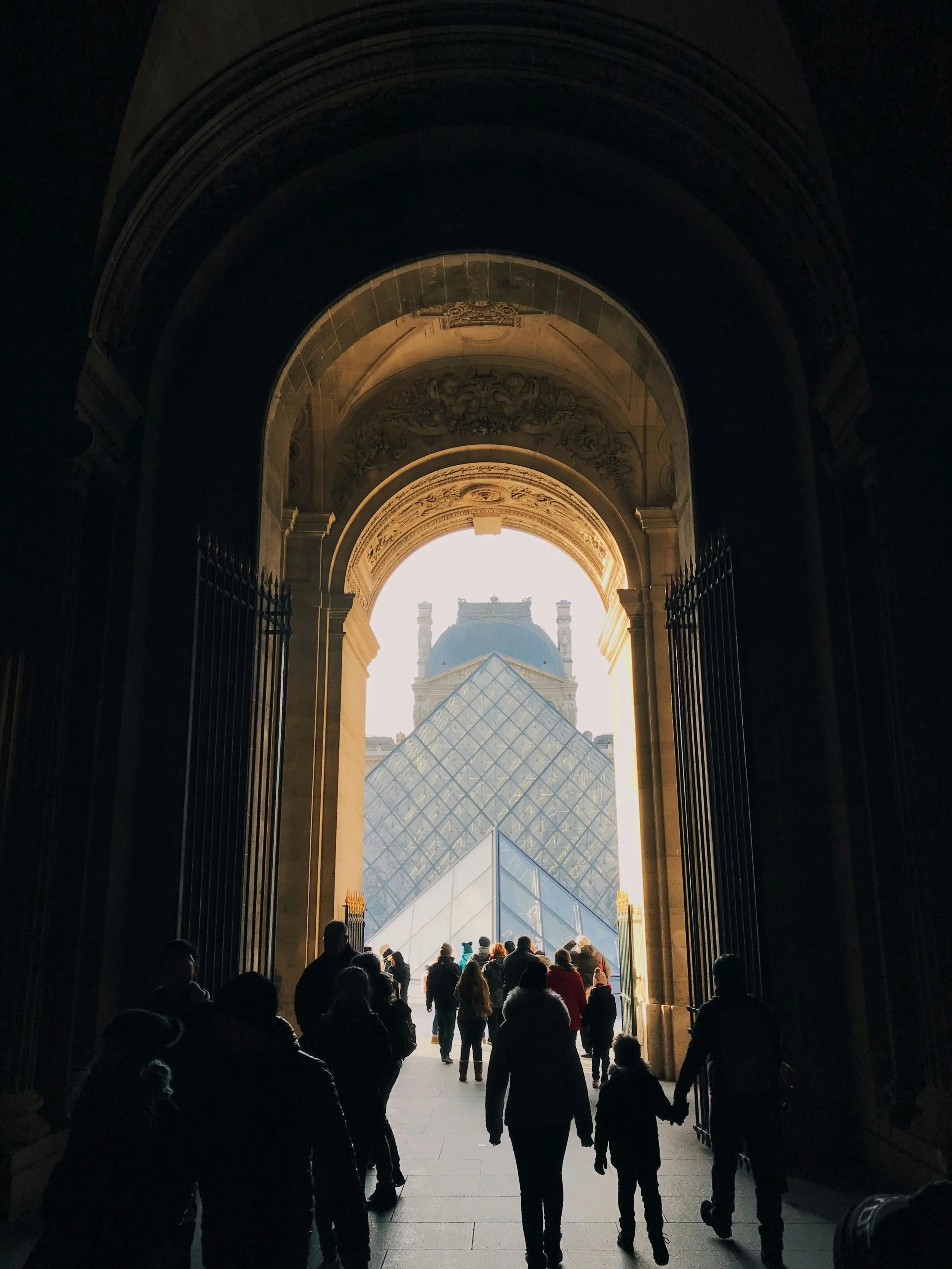 vue d'une entrée ou d'une sortie avec plusieurs personnes qui entrent ou sortent, avec le monument du Louvre et sa pyramide visible en arrière-plan.