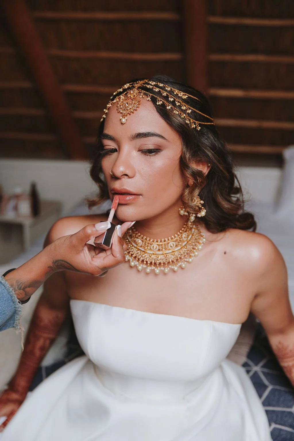 A bride with jewelry is getting her makeup finished, with a makeup artist applying lipstick