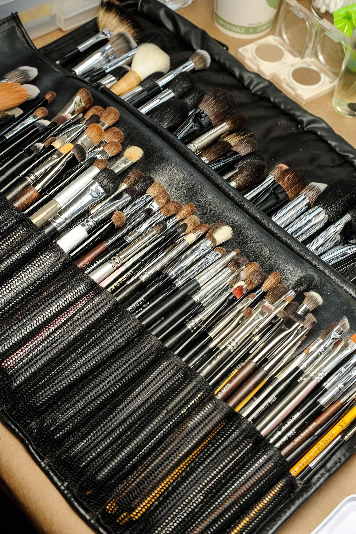 A black makeup brush roll opens to reveal multiple rows of makeup brushes of various sizes and shapes.
