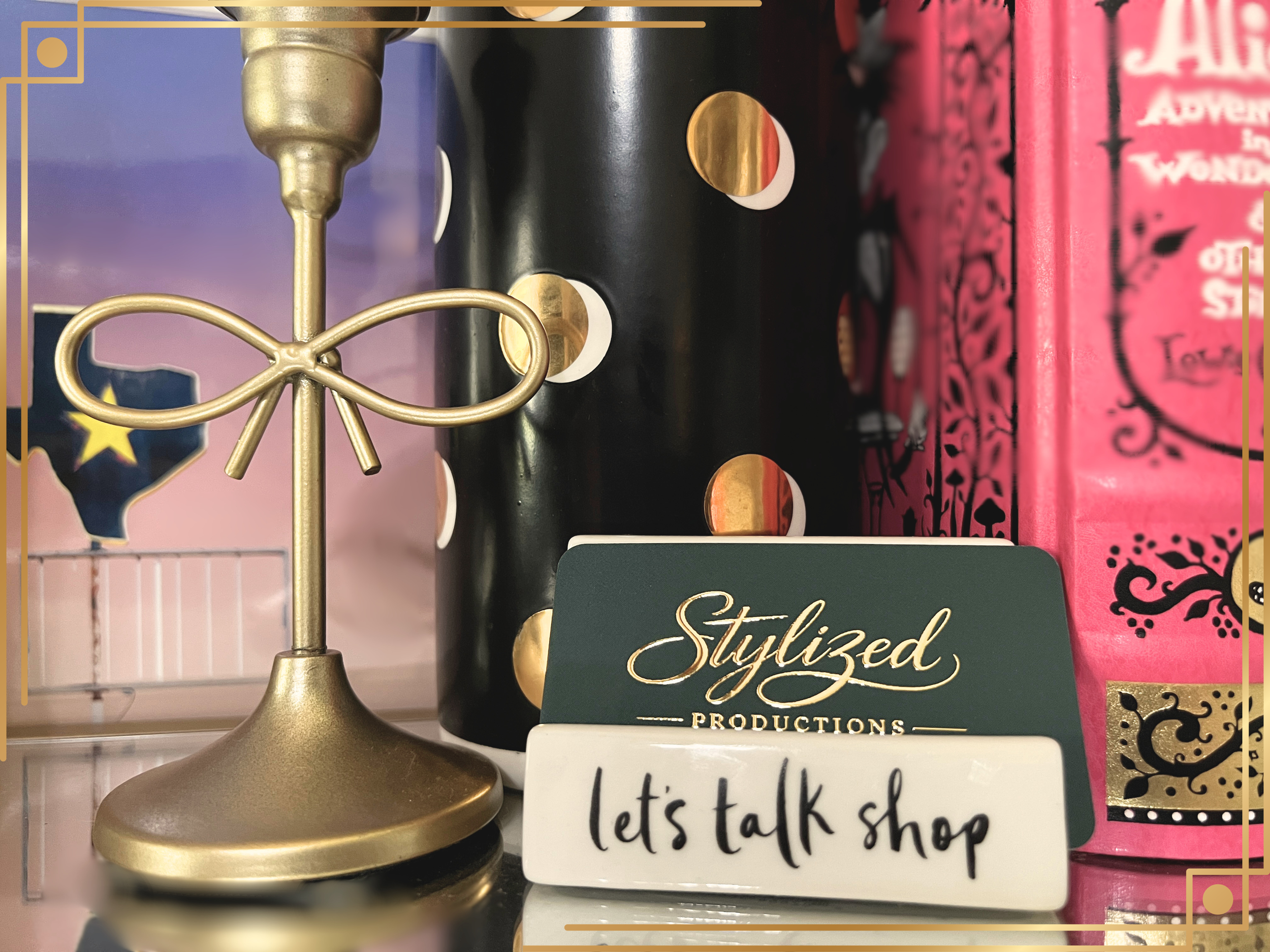 A decorative brass or gold-colored table lamp with a bow shaped detail on the stand, positioned next to a sign that reads 'Styled Productions' and a handwritten note that says 'Let's talk shop'.