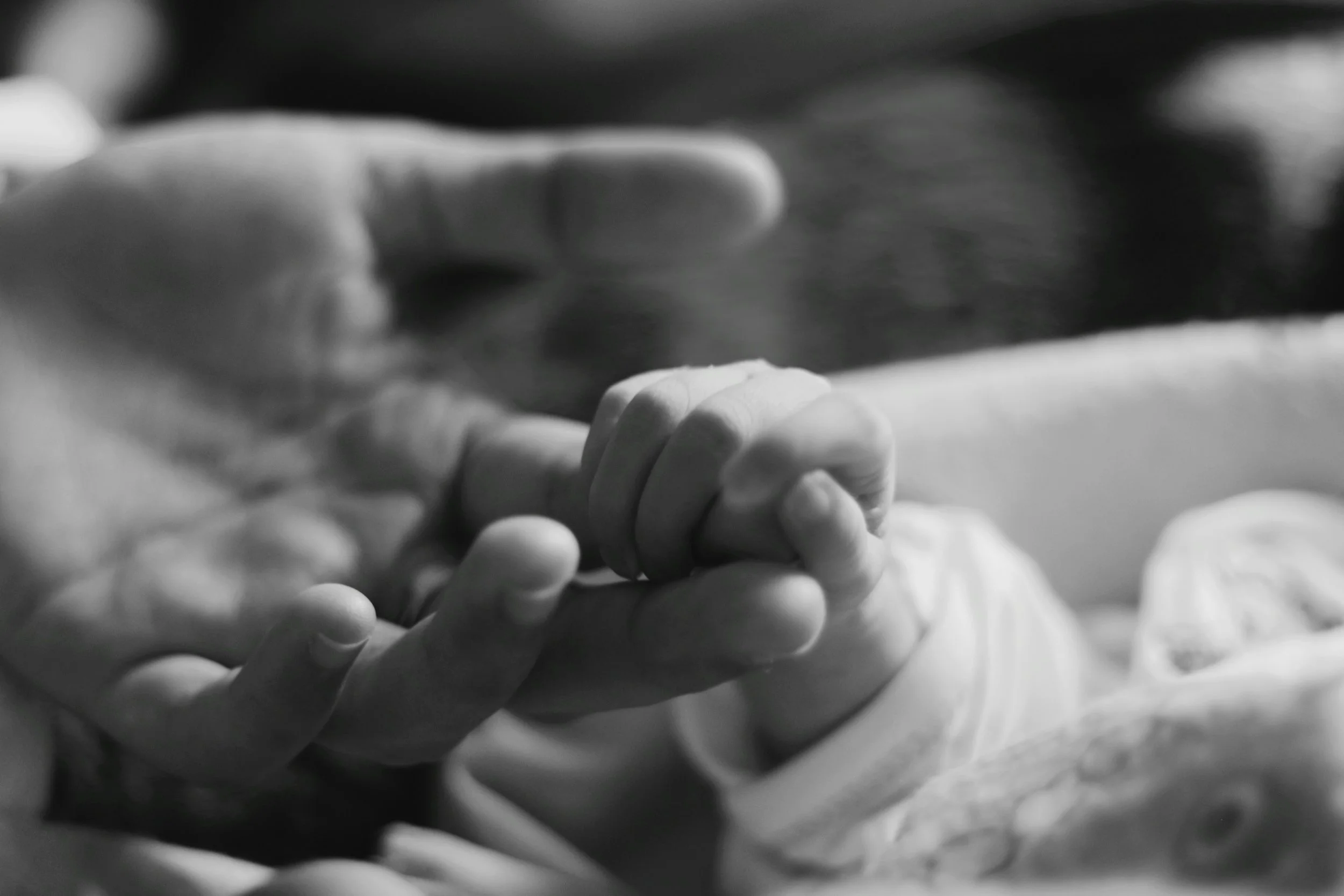 Close-up of a newborn baby gently gripping an adult’s finger, symbolizing care, support, and connection.