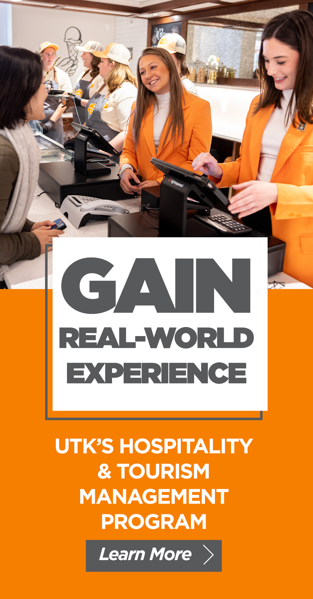 People dressed in orange blazers and uniforms at a hospitality service counter, interacting with a customer in a restaurant or cafe setting.
