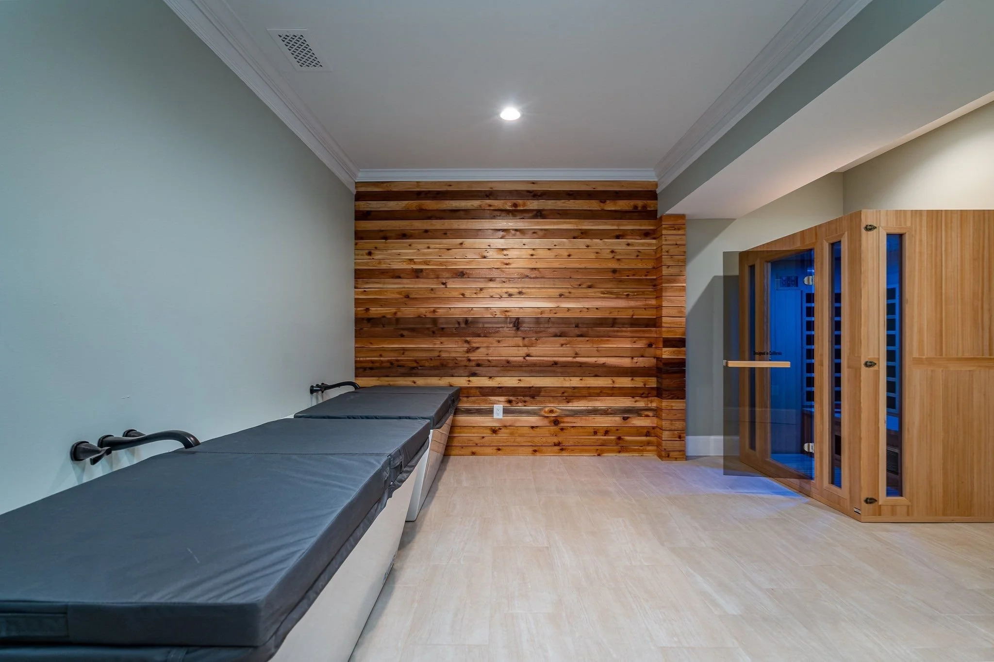 Room with wooden wall panel, medical bed with black mattress, and a wooden sauna or cabinet on the right side.