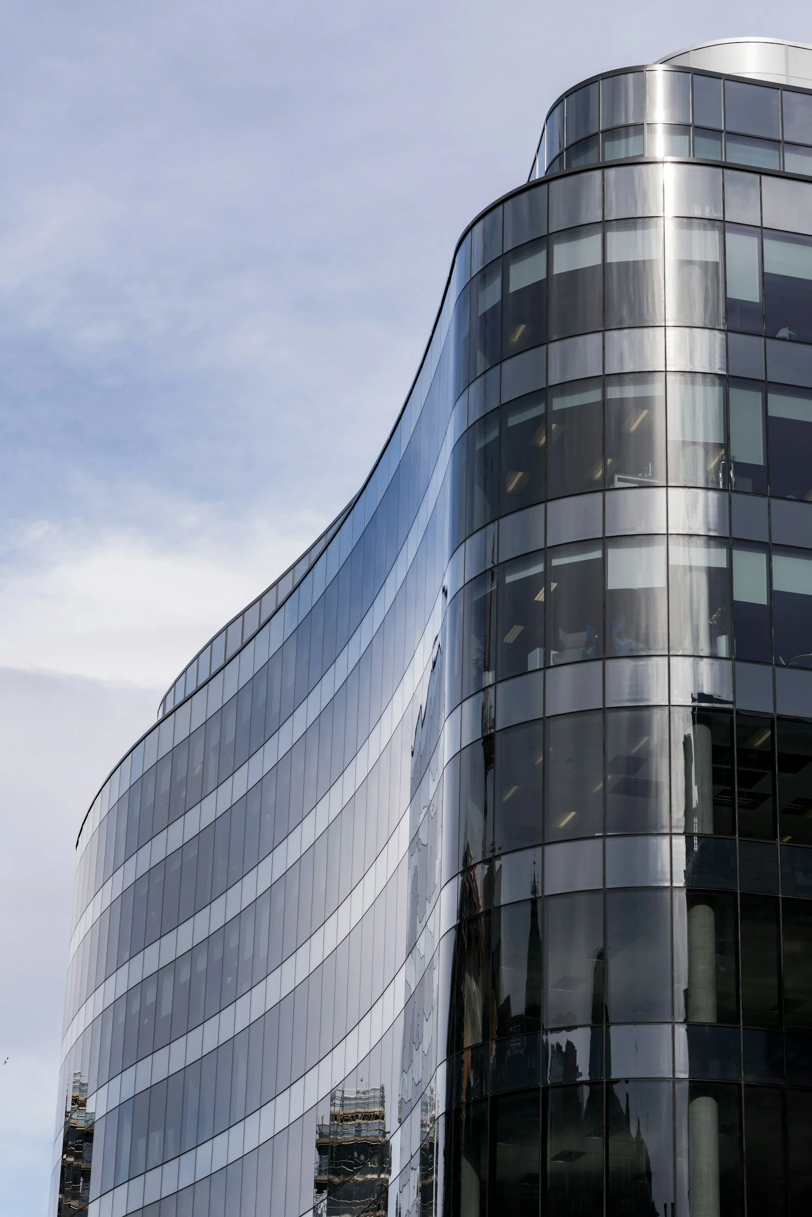 Modern glass office building with curved edges and reflective exterior, against a cloudy sky.