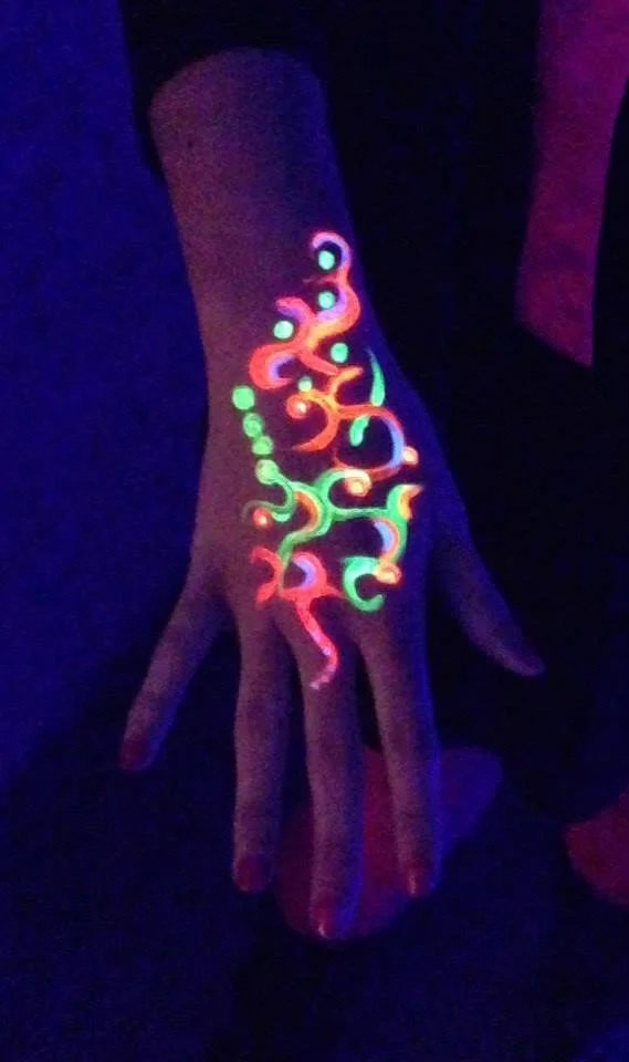 Maquillage UV fluo sur la main, motif lumineux sous lumière noire.