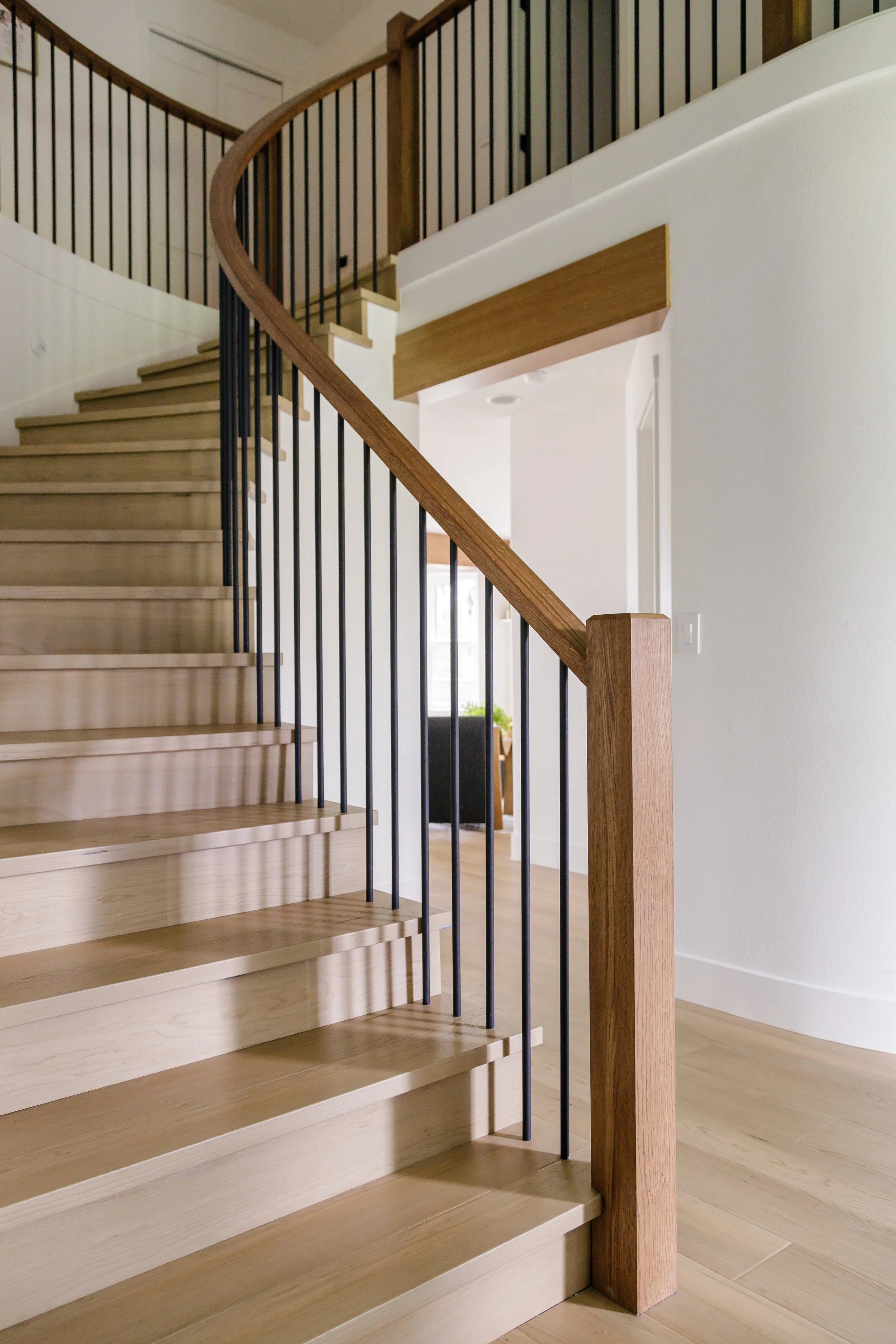 A wooden staircase with black metal balusters and a wooden handrail inside a modern home.