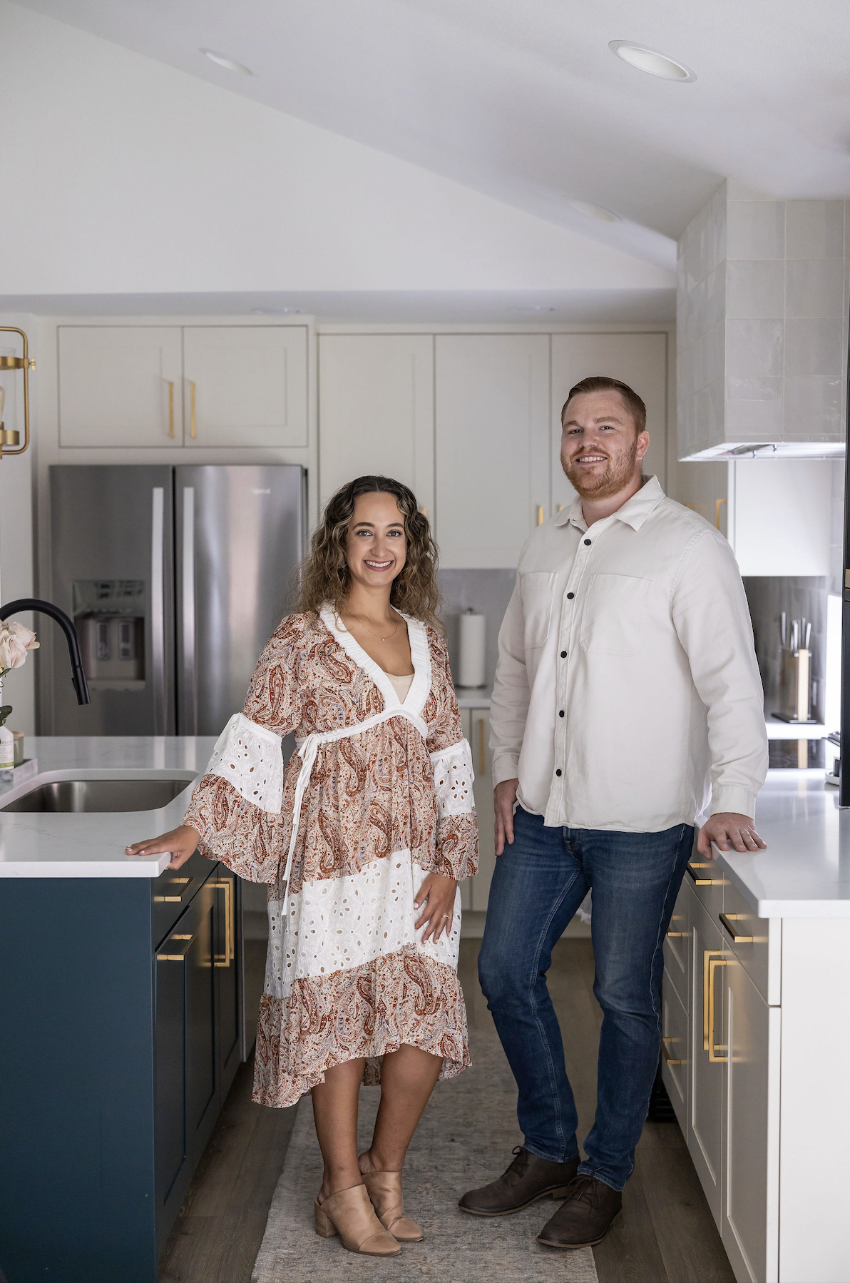 A woman and a man standing in a modern kitchen, smiling at the camera.