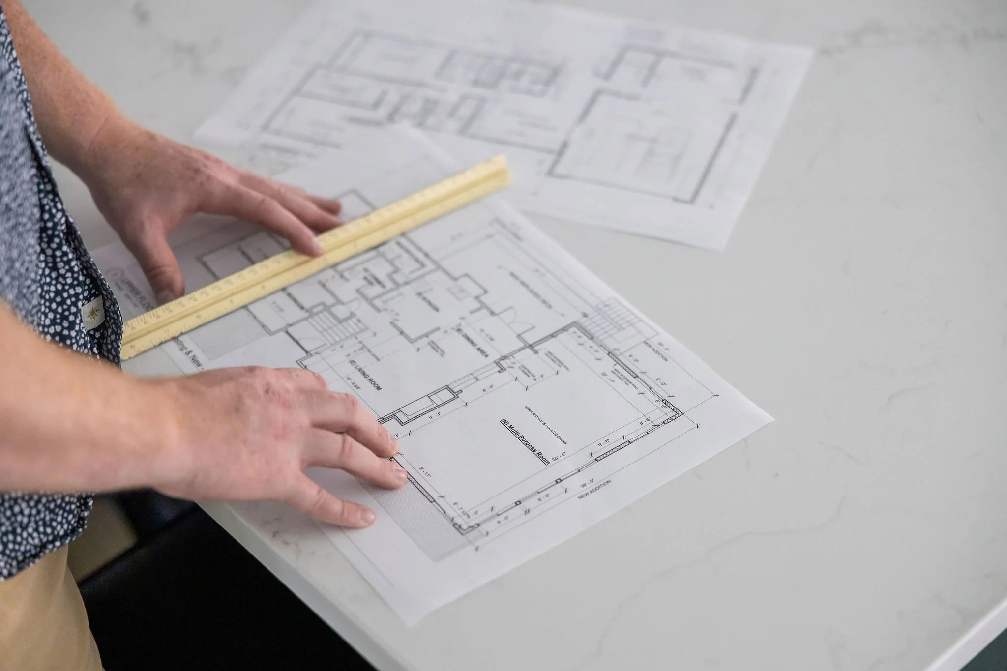 Hands measuring a blueprint of a building on a white table.