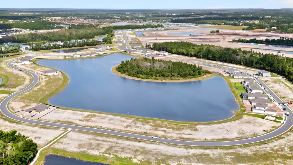 Aerial view of New Smyrna Beach's newest community, Ardisia Park, with a large lake, surrounded by houses, trees, and a curved road.