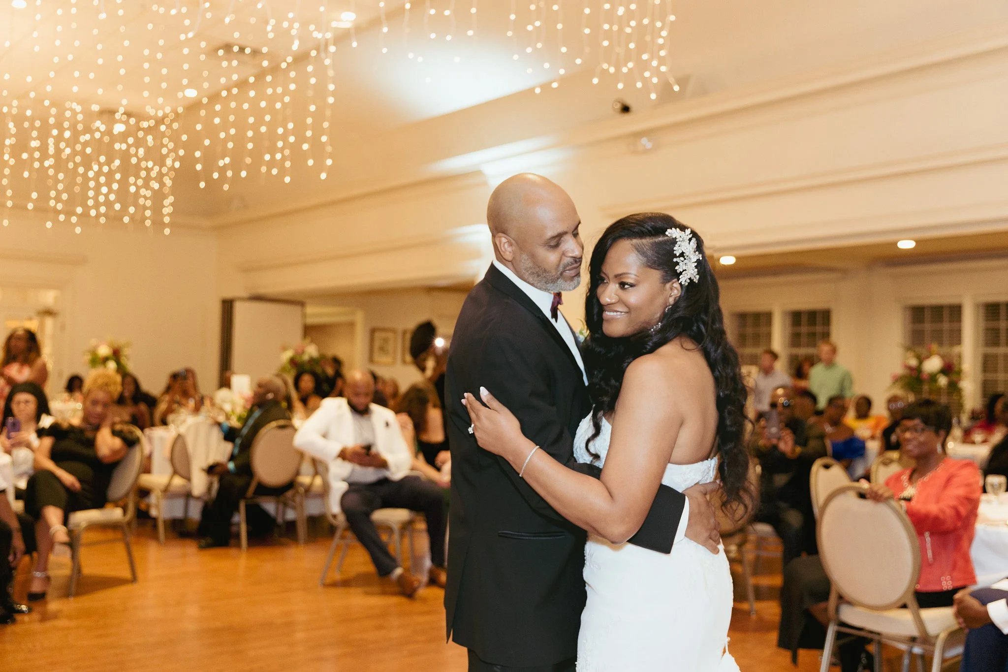 A bride and groom sharing their first dance at their wedding reception, surrounded by seated guests in a decorated banquet hall.