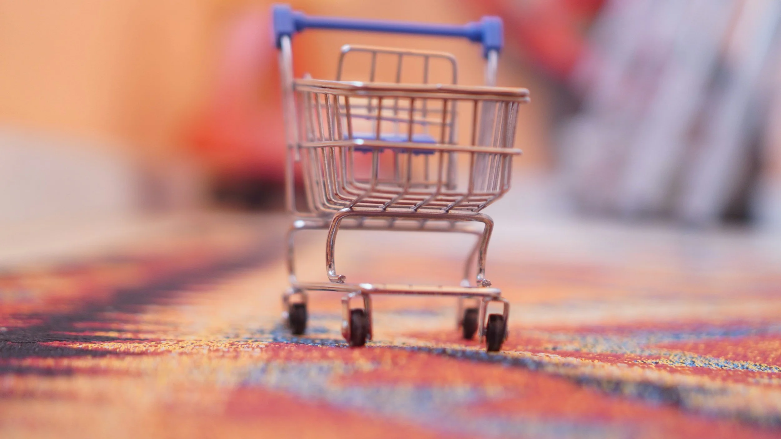 Small shopping cart toy placed on a colorful patterned surface with blurred background.