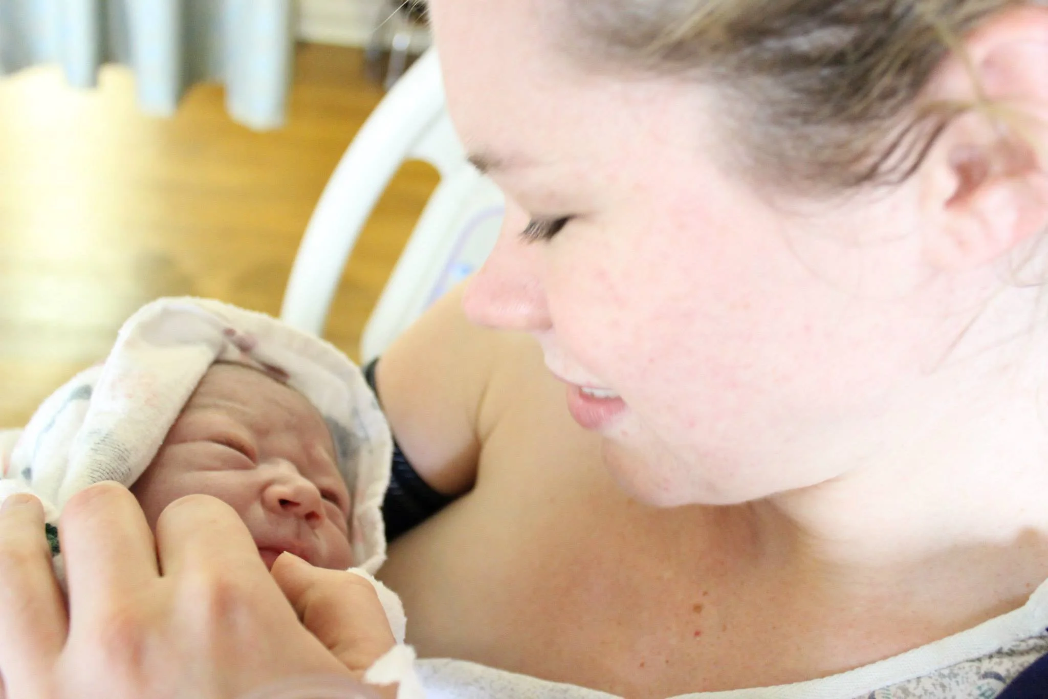 A mother holding her newborn baby in a hospital bed, gazing lovingly at the infant.
