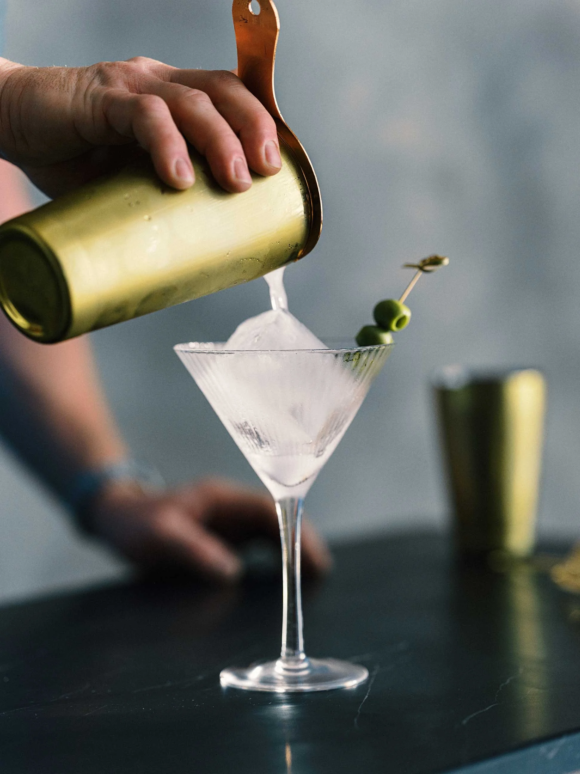 martini being poured from a bottle with olive garnish in a chilled glass