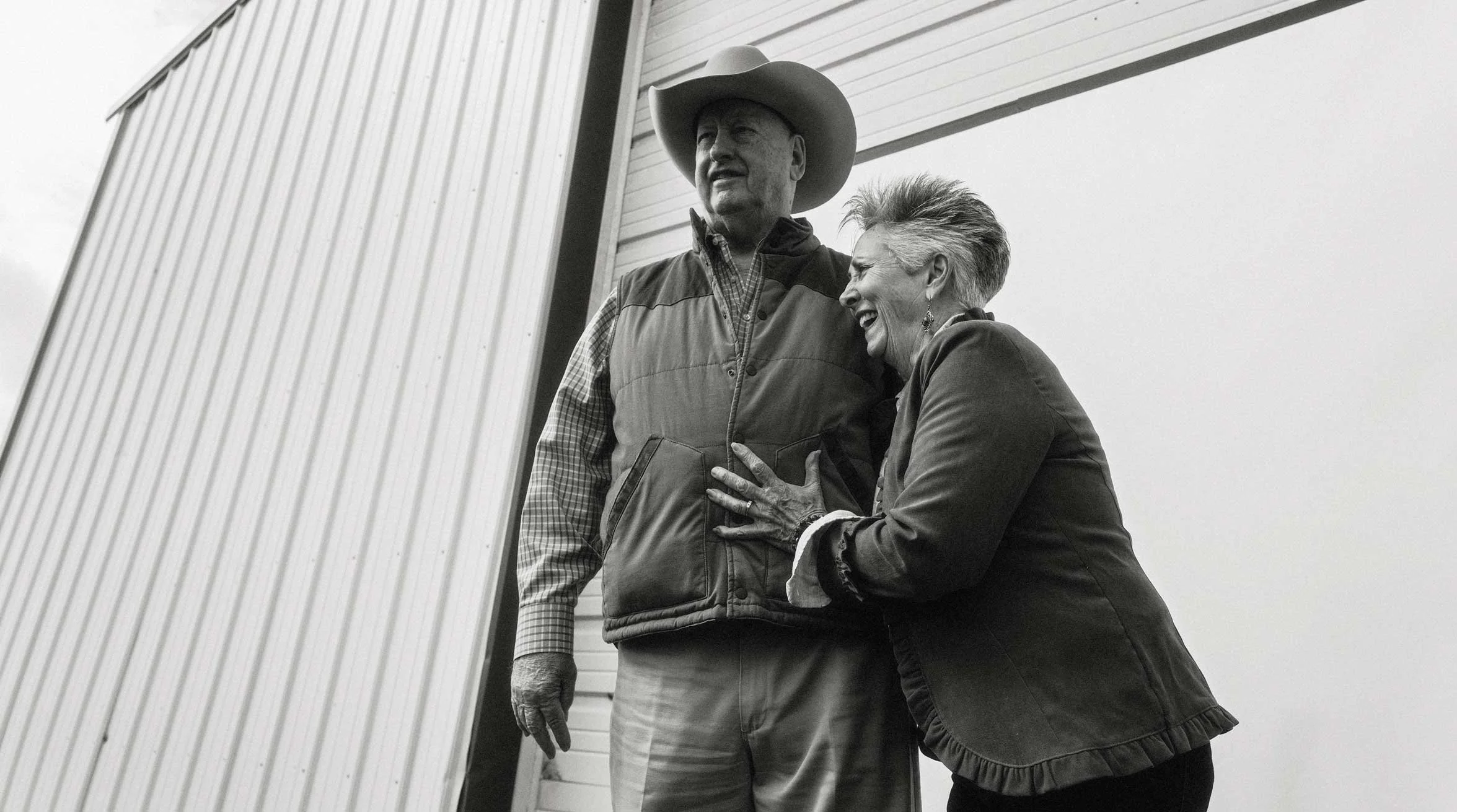 rancher standing with a short haired woman outside a barn