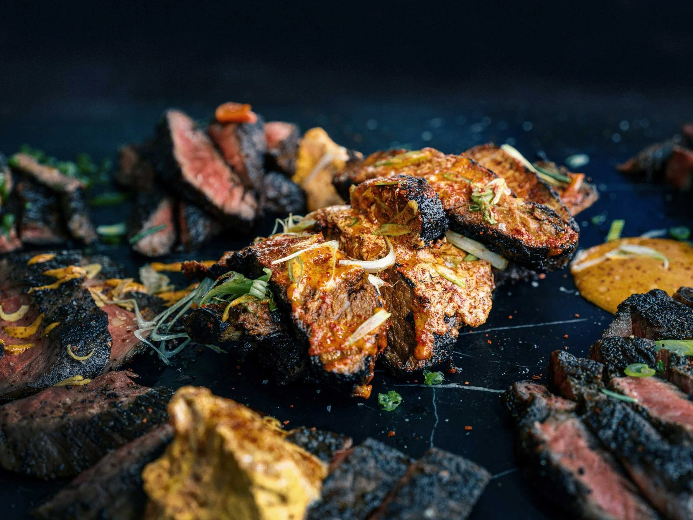 grilled steak and roasted meat plated on a dark surface with herbs and seasoning