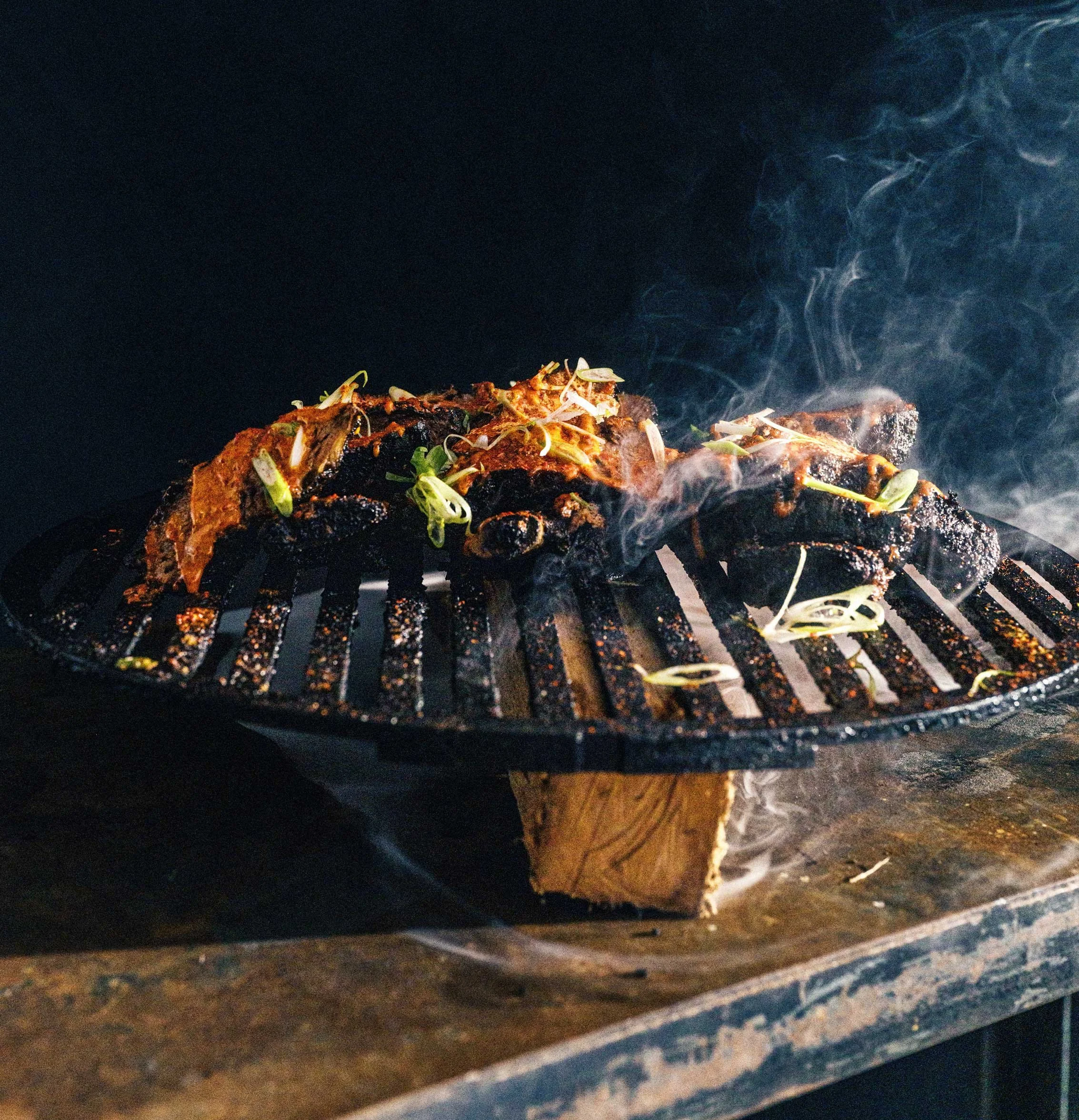 steak cooking over an open flame grill with smoke rising