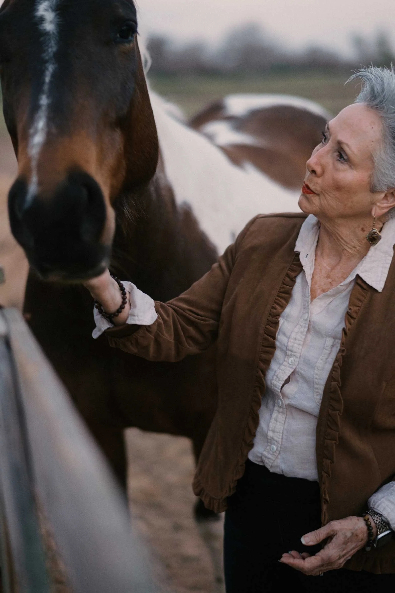 woman gently holding a horse’s face in a stable