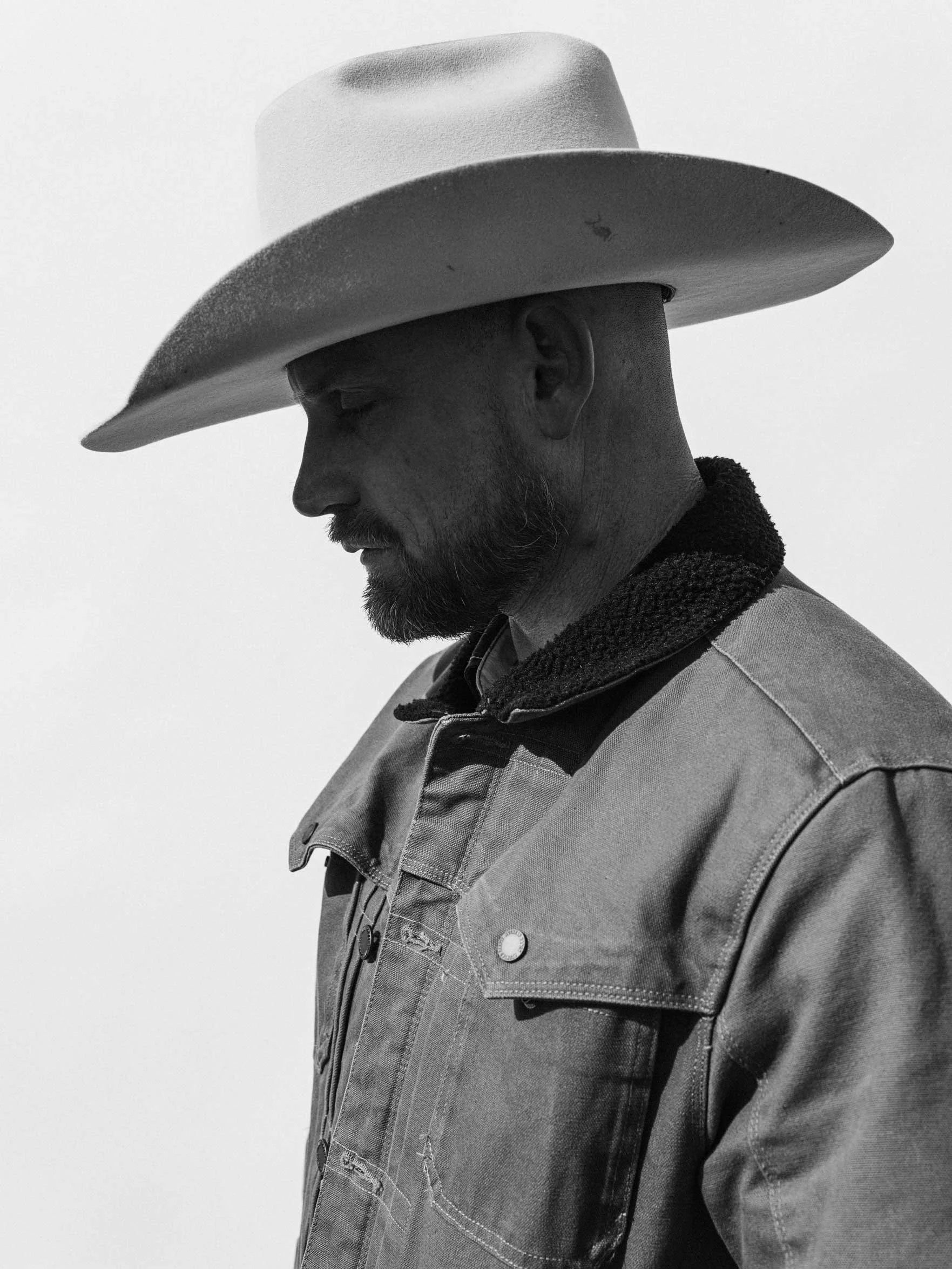 black and white portrait of a cowboy looking down wearing a wide brim hat