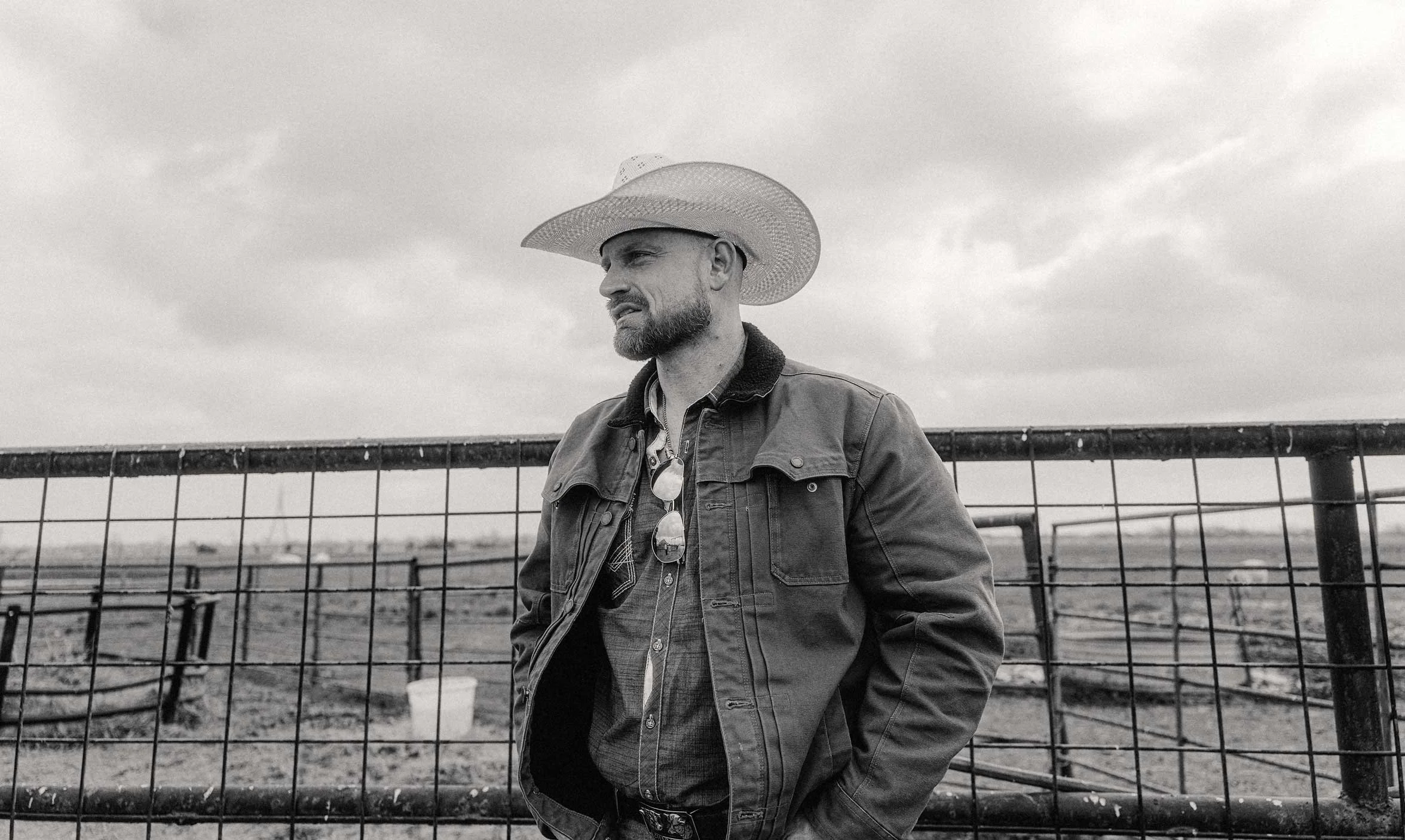 black and white portrait of a cowboy standing by a ranch fence