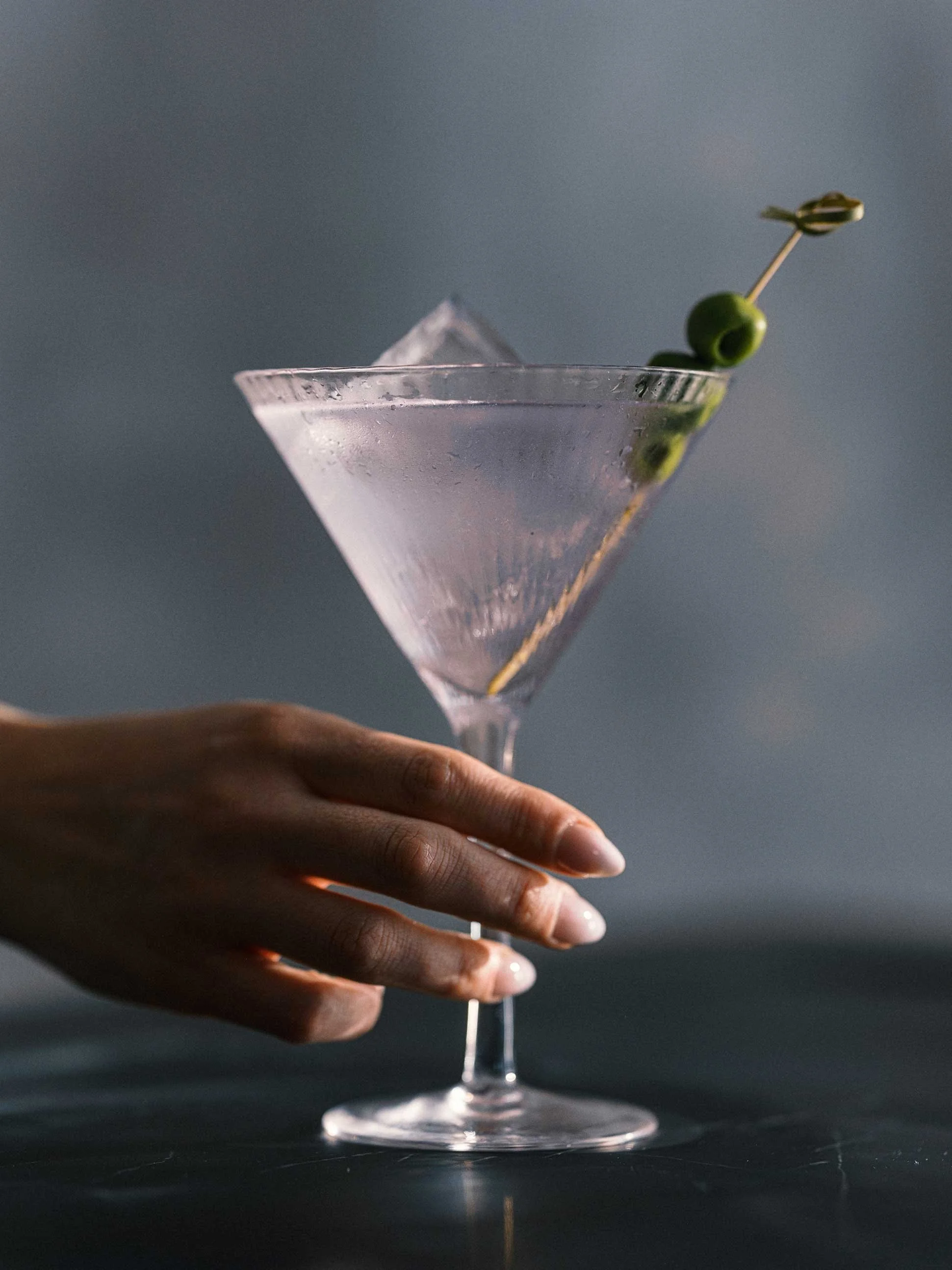 hand holding a martini glass with olive garnish
