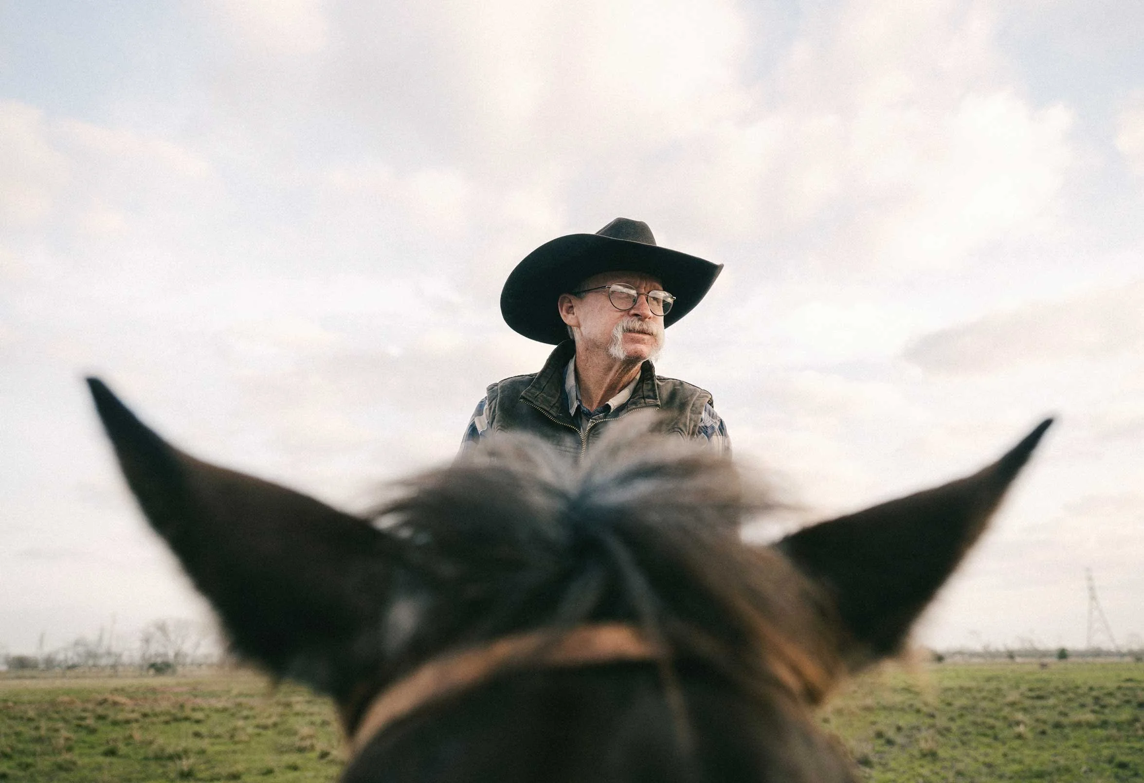 cowboy riding a horse viewed from behind the horse’s ears